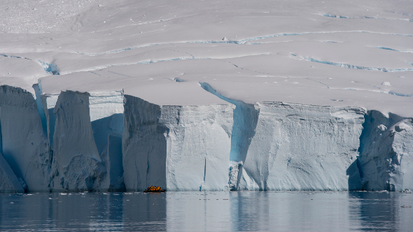  a small explorer boat  infront of a large ice shelf